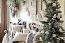 a neutral Christmas entryway with a tree with white ornaments, lots of printed pillows, evergreens and pinecones