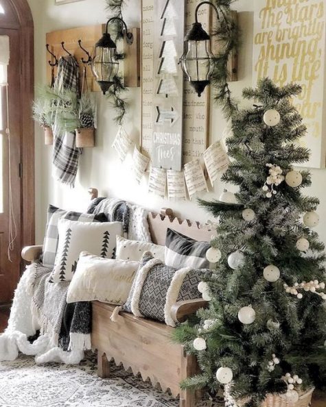 a neutral Christmas entryway with a tree with white ornaments, lots of printed pillows, evergreens and pinecones