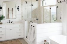 a neutral farmhouse bathroom clad with shiplap, a wooden vanity, a free-standing tub and touches of black
