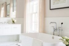 a refined neutral bathroom with a white tub, vanity and tiles, a wooden bench and blush curtains