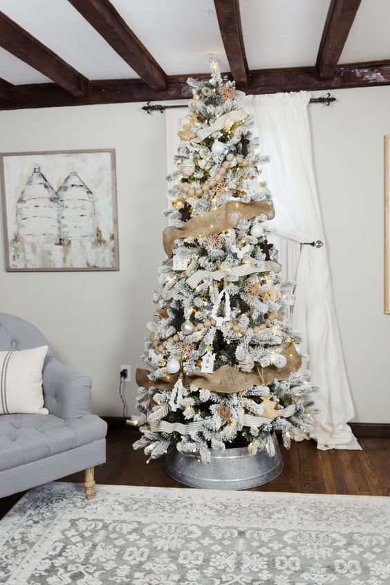 a rustic flocked Christmas tree with burlap ribbon, lights, white and metallic ornaments placed into a metal surround