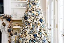 a shiny and catchy flocked Christmas tree with metallic and blue ornaments, lights and ribbons is a chic idea