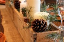 a simple rustic Christmas centerpiece of a wooden box with pinecones, evergreens and pillar candles