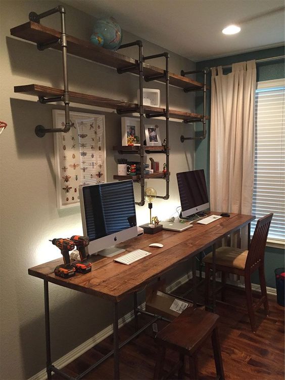 a small industrial shared home office with a large shelving unit with pipes, a mathcing desk and wooden chairs
