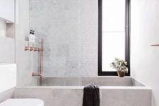 a small neutral bathroom with a tile clad tub, copper fixtures and a hex tile wall for a chic look