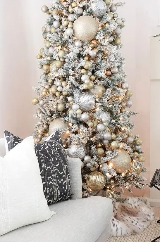 a snowy Christmas tree with oversized and smaller metallic Christmas ornaments plus lights