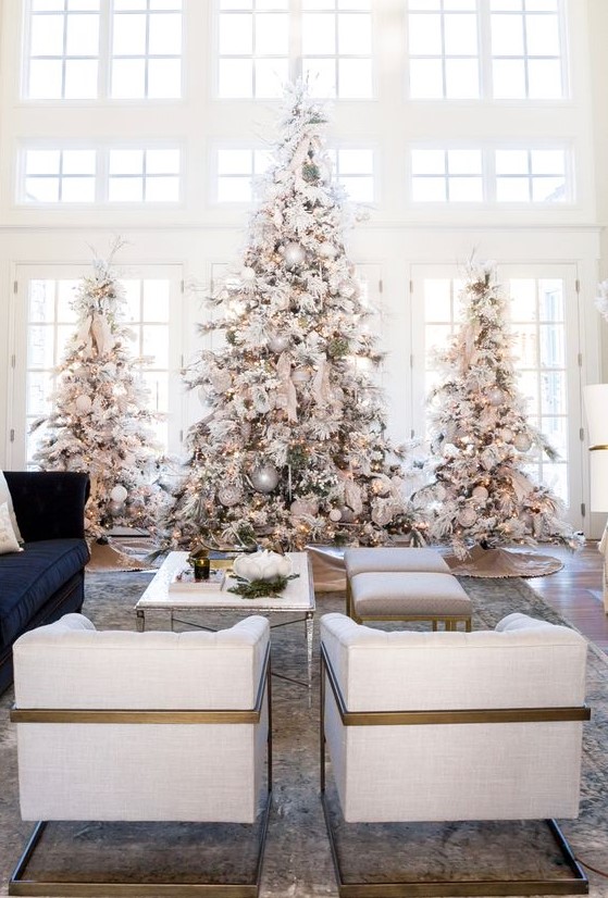 a trio of large flocked Christmas trees with lights, neutral and metallic ornaments for a winter fairy tale in the space