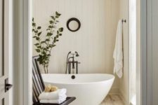 a warm-colored bathroom clad with shiplap, with some dark touches and a free-standing tub