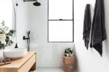 a white minimalist bathroom with a seamless shower space, a wooden vanity and stool and touches of black for drama