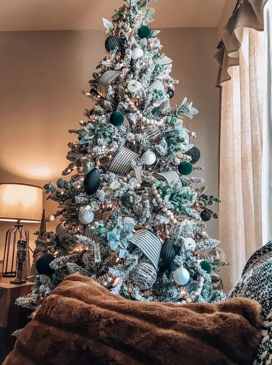 an elegant flocked Christmas tree decorated with white, black and dark green ornaments, leaves, ribbons and wooden beads