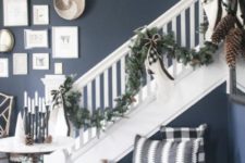 plaid and striped pillows, an evergreen garland with bows, candles and pinecones for a Christmas space