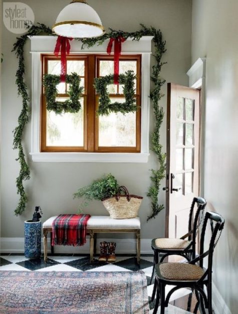 square evergreen wreaths, an evergreen garland, a plaid blanket for a stylish holiday entryway