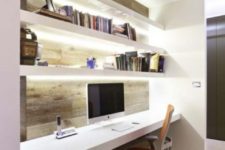 03 a minimalist workspace with a wood clad wall, white floating shelves with built-in lights and a matching desk plus a comfy chair