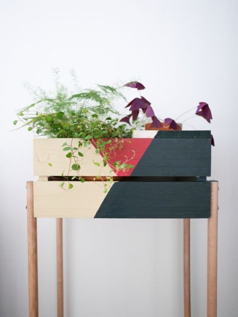 a color block Knagglig box placed on wooden legs acts as a plant stand or a large planter
