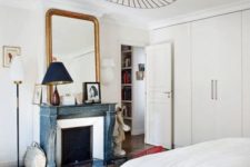 12 a neutral Parisian bedroom with a blue non-working fireplace, a statement lamp, a chic mirror and an antique wooden chair