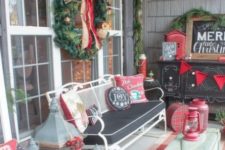 16 a vintage Christmas porch in red, white and black with comfy furniture and colorful pillows, skates, an evergreen wreath and evergreens all around
