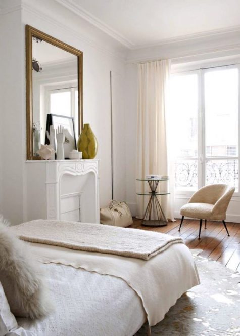 a chic neutral Parisian bedroom with a faux fireplace, a statement mirror, a neutral chair and a large bed