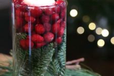 19 a chic and simple holiday centerpiece of a tall glass with evergreens, cranberries and a floating candle