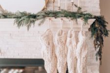 20 evergreens, simple candles in gold candleholders and white knit stockings on the mantel for a minimal holiday look