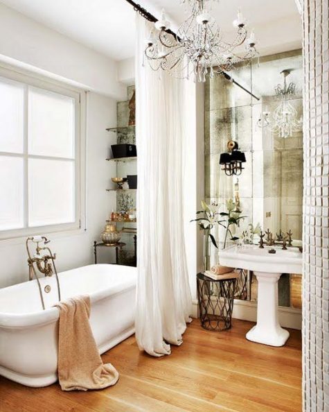 a refined Parisian bathroom with a mirror wall, a crystal chandelier, a tub, open shelves and a sink
