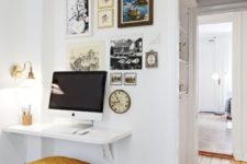 23 a white floating mini desk and a stool with a pillow, a gallery of artworks and a wall lamp for working