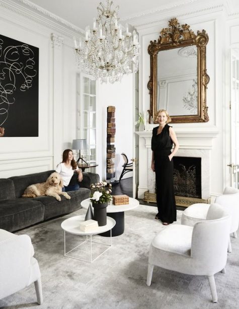 a sophisticated Parisian living room with white walls, soft velvet furniture, a fireplace, a statement mirror and chandelier