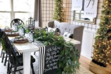 a chic farmhouse Christmas dining room with tall Christmas trees, a greenery runner, a striped and chalkboard runner, signs and candles