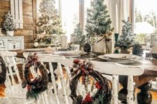 a farmhouse Christmas dining space with whitewashed chairs, snowy Christmas trees and pinecones