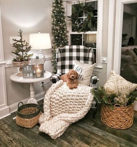 a farmhouse Christmas nook with baskets, evergreens and lights, a buffalo check chair and a chunky knit blanket