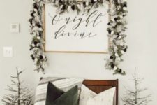 a farmhouse Christmas space with a snowy evergreen garland, snowy Christmas trees, a green and white pillow and a cozy blanket