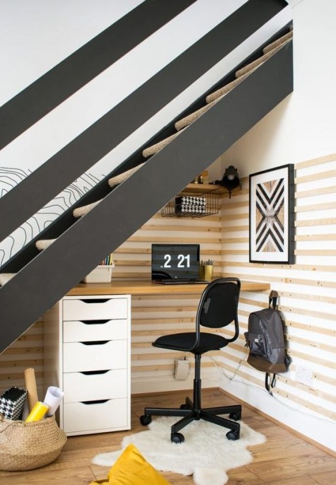 a modern rustic under the stairs home office with a built-in desk with storage drawers, a black chair, a rug and a basket for storage