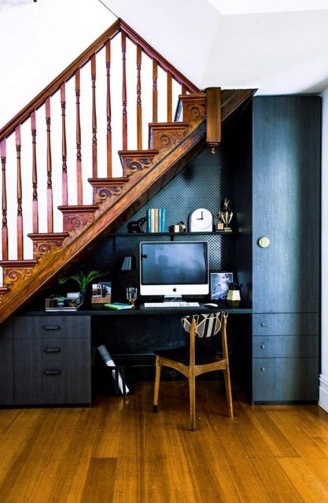 an elegant dark home office with much storage space, a built-in desk, a small chair and a shelf