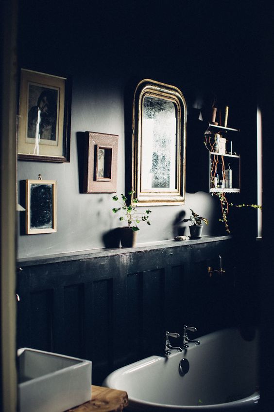 a dark vintage-inspired bathroom with a gallery wall, a bookshelf and a free-standing tub for a moody feel