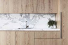 22 a stylish minimalist kitchen of light-colored wood, with a marble backsplash and no handles