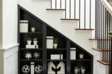 a black storage unt with open shelves and cabinets right into the staircase