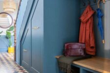 a blue under stairs mudroom with built-in drawers, a built-in bench and a cabinet, a pallet and some lights