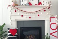 a chic Valentine fireplace with red and white pompoms garlands, heart throws, a couple of signs and red and white decor on the wall