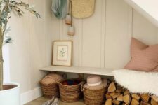 a cozy farmhouse under stairs mudroom with a built-in bench, some firewood, baskets and a potted plant is a very cool space