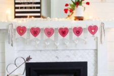 a modern Valentine fireplace with a pink heart garland, candles, pink tulips and a striped sign