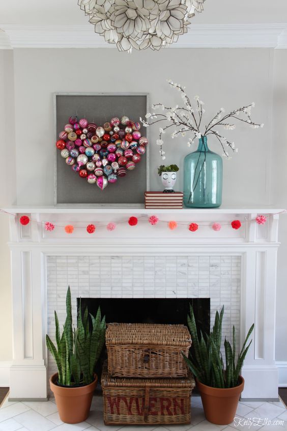 a simple Valentine mantel with a colorful ornament heart, blooming branches and a red pompom garland