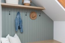 a small and cool under stairs mudrom with a pale blue wall, a built-in storage bench, a shelf with baskets and some pillows