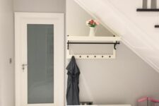 a small modern mudroom under the stairs with a storage seat, a rack and some decor is a cool idea for a tiny space