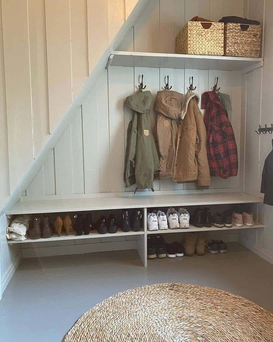 a small under stairs mudroom with built-in shelves, racks and baskets for storage plus a jute rug is a cool idea