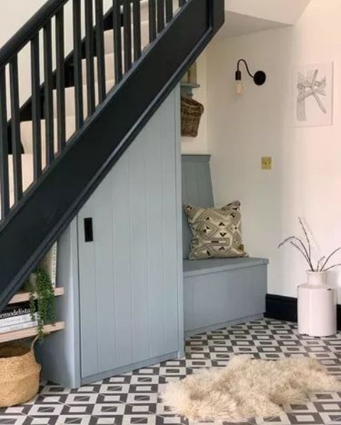 a tiny mudroom under the stairs with a light blue wardrobe, a built-in bench with storage, baskets and some cute decor
