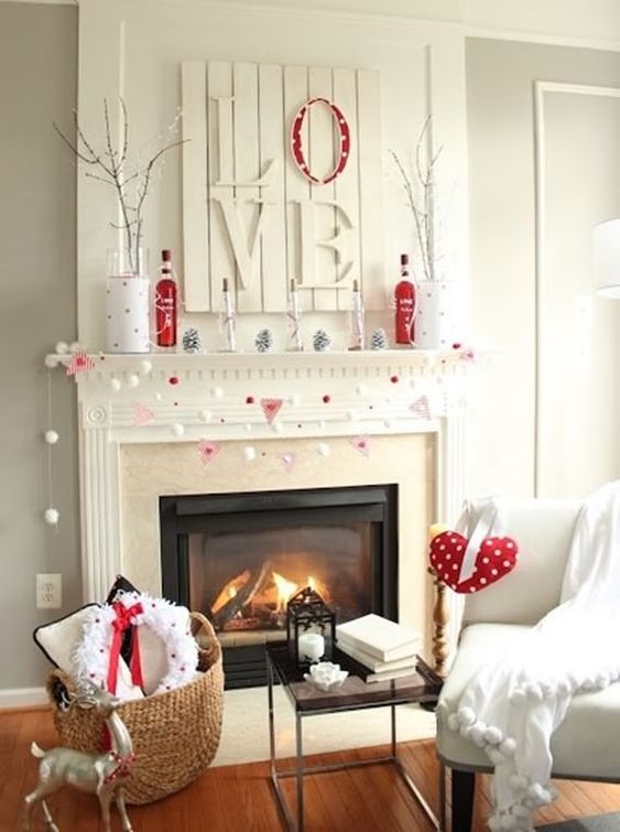 a white and red Valentine mantel with a LOVE sign, red and white pompoms, branches in vases and white pinecones