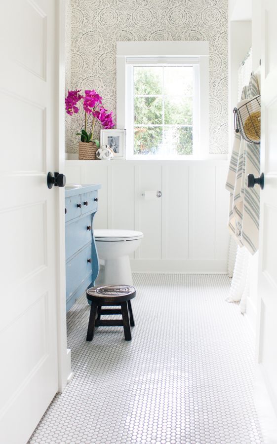 a cozy traditional bathroom with a white penny tile floor, wainscoting and a blue dresser looks cool