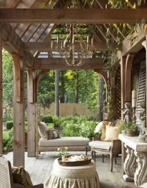 a French country chic neutral terrace with a refined chandelier, wooden furniture with upholstery and lots of greenery