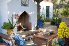 a Mediterranean patio done with a large fireplace decorated with azulejo tiles, vintage wooden furniture and bright blooms