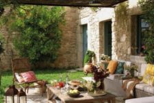 a Mediterranean terrace with bright throws, ottomans, floor cushions, wooden furniture and potted blooms and greenery