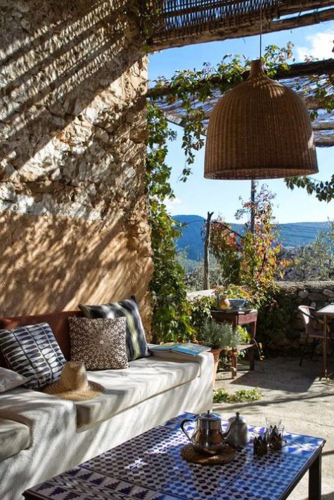 a Mediterranean terrace with stone walls, wicker lampshades, bright printed throws, a mosaic tile table and rattan chairs